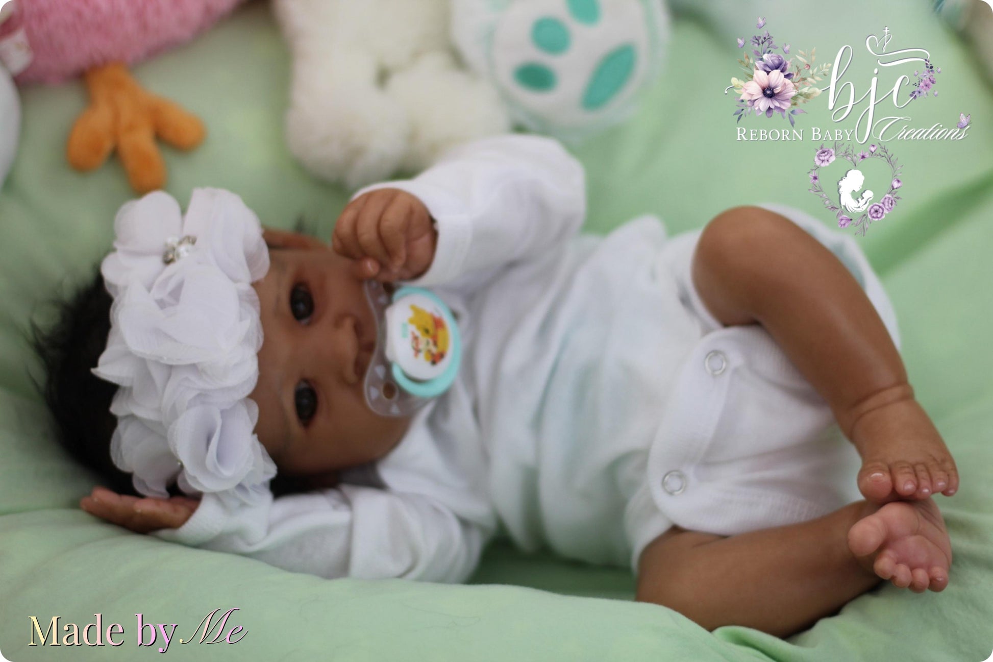 A handmade baby doll with a white outfit and a flower headband lying on a green bedspread.