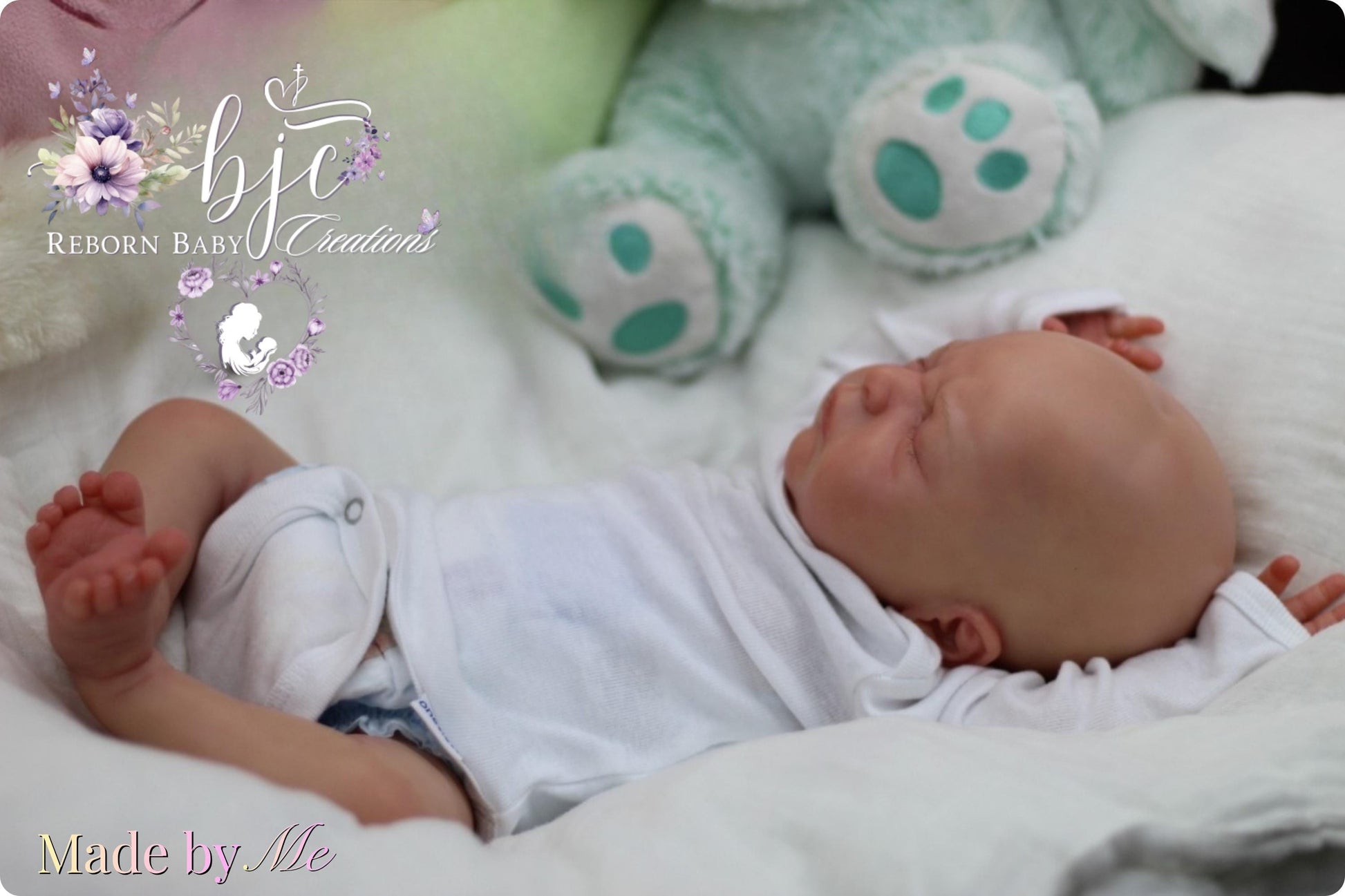 A newborn baby is peacefully sleeping on a bed, surrounded by a white blanket and a stuffed animal.
