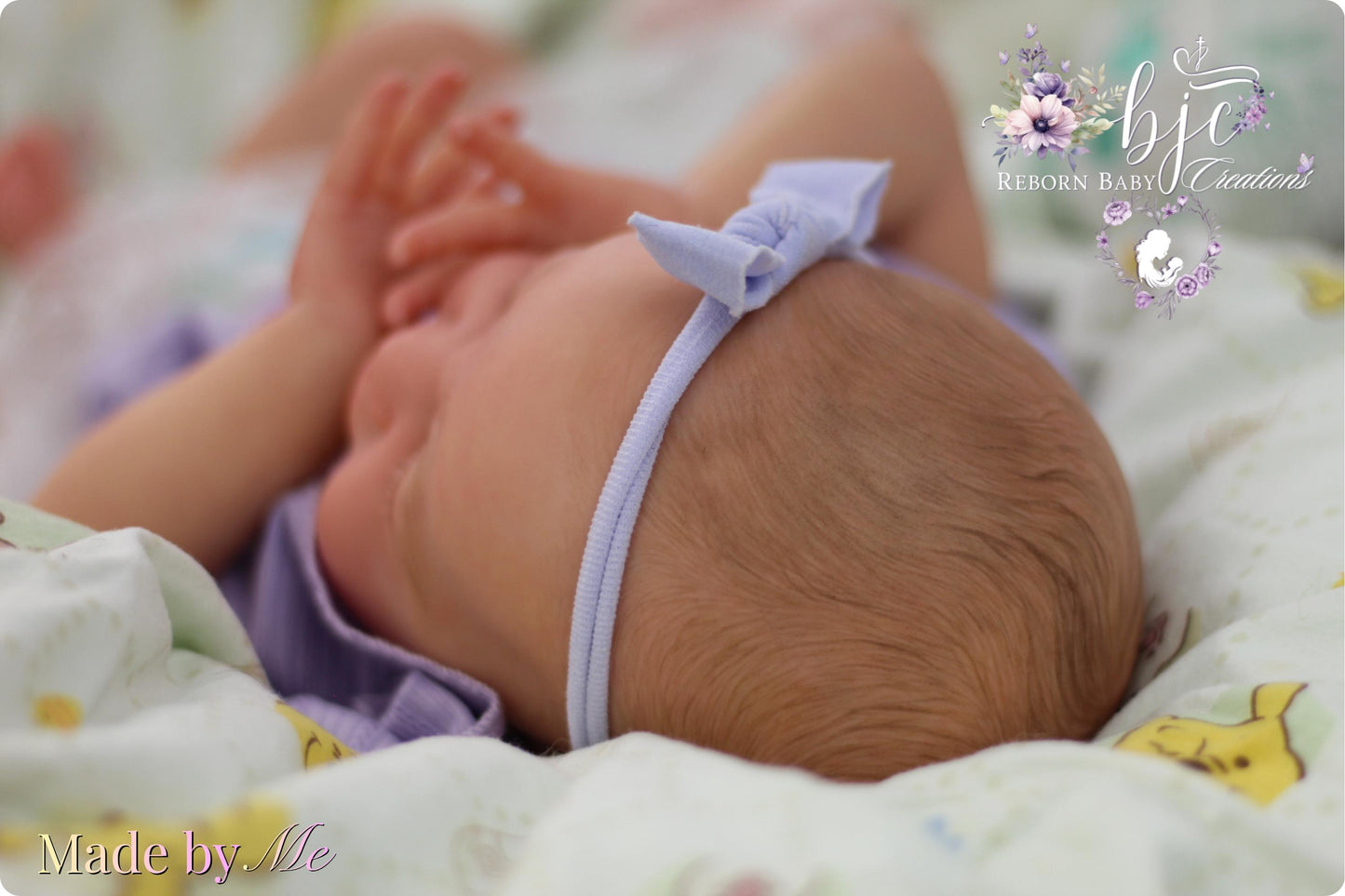 A newborn baby girl wearing a purple headband is lying on a bed with a floral patterned blanket.