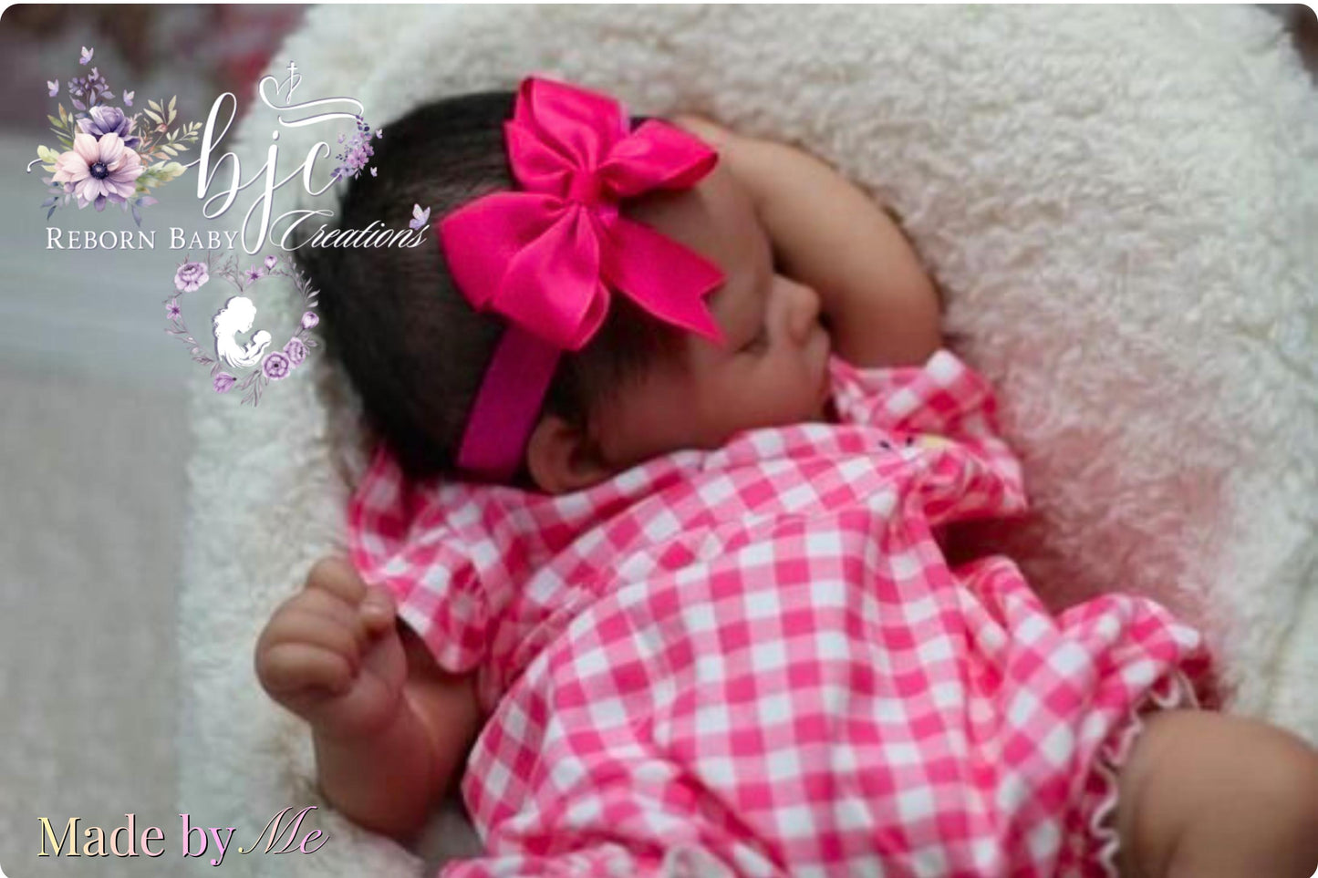 A newborn baby girl wearing a pink bow and a pink and white checkered dress is peacefully sleeping in a white blanket.